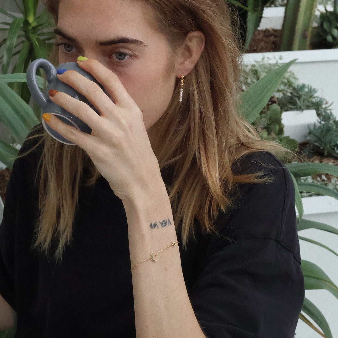 Thea bracelet worn solo on wrist, showcasing star and moon charms on a delicate gold chain