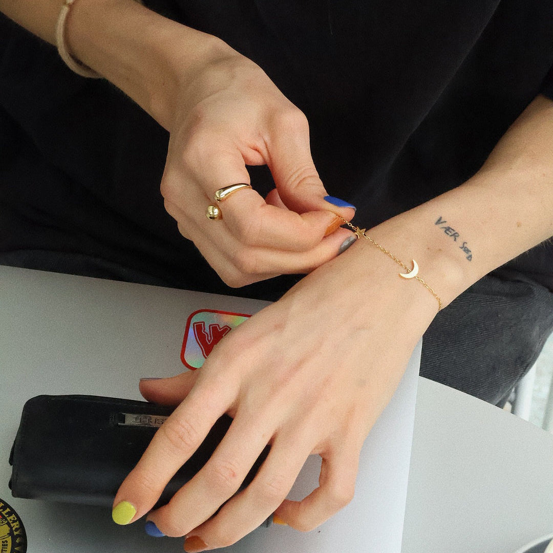 Thea bracelet worn solo on wrist, showcasing star and moon charms on a delicate gold chain