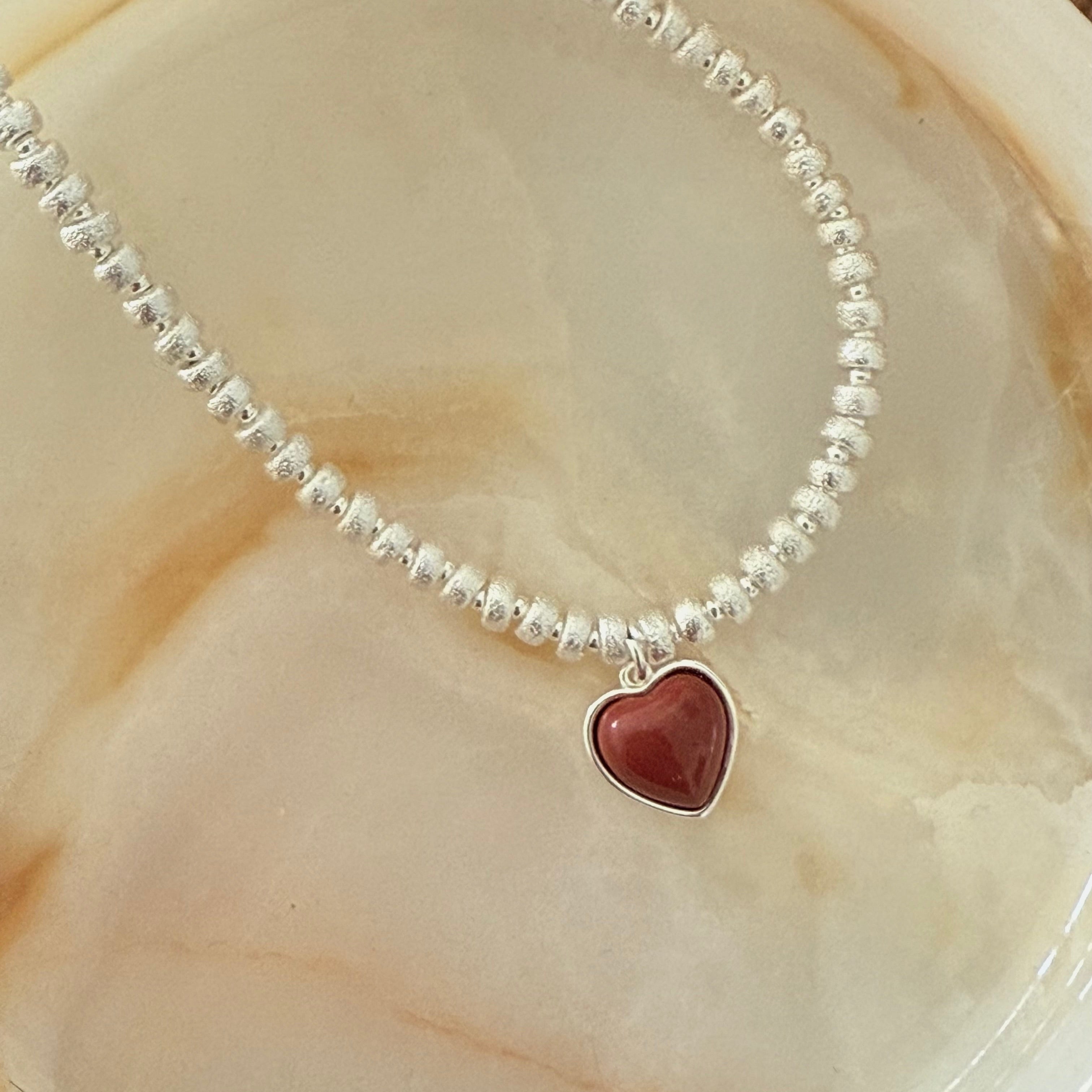 Close-up of Liora's wine red heart pendant against the matte white gold bead chain