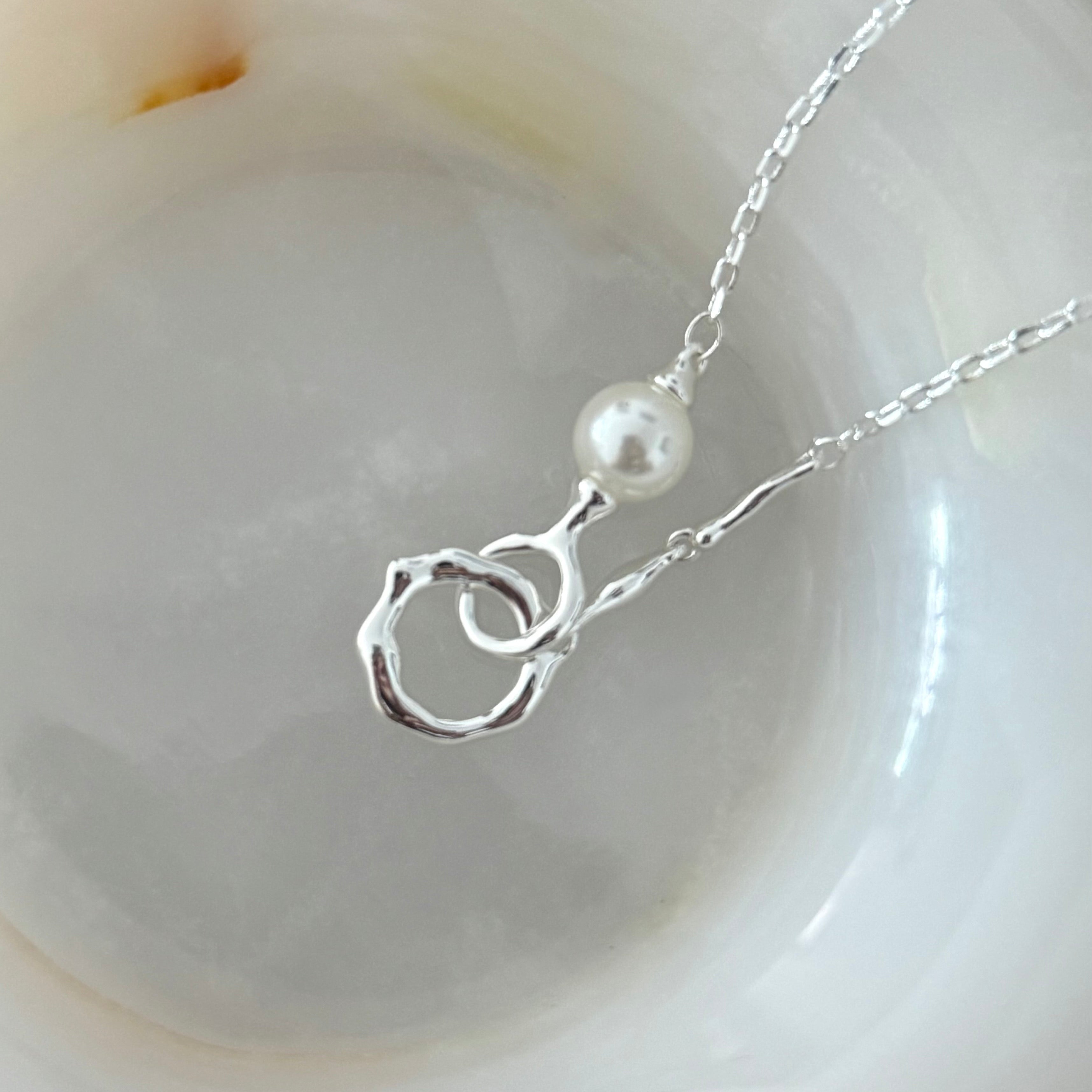 The Sonnet necklace in 18K white gold plating worn alone, featuring textured double ring pendant with freshwater pearl on delicate chain