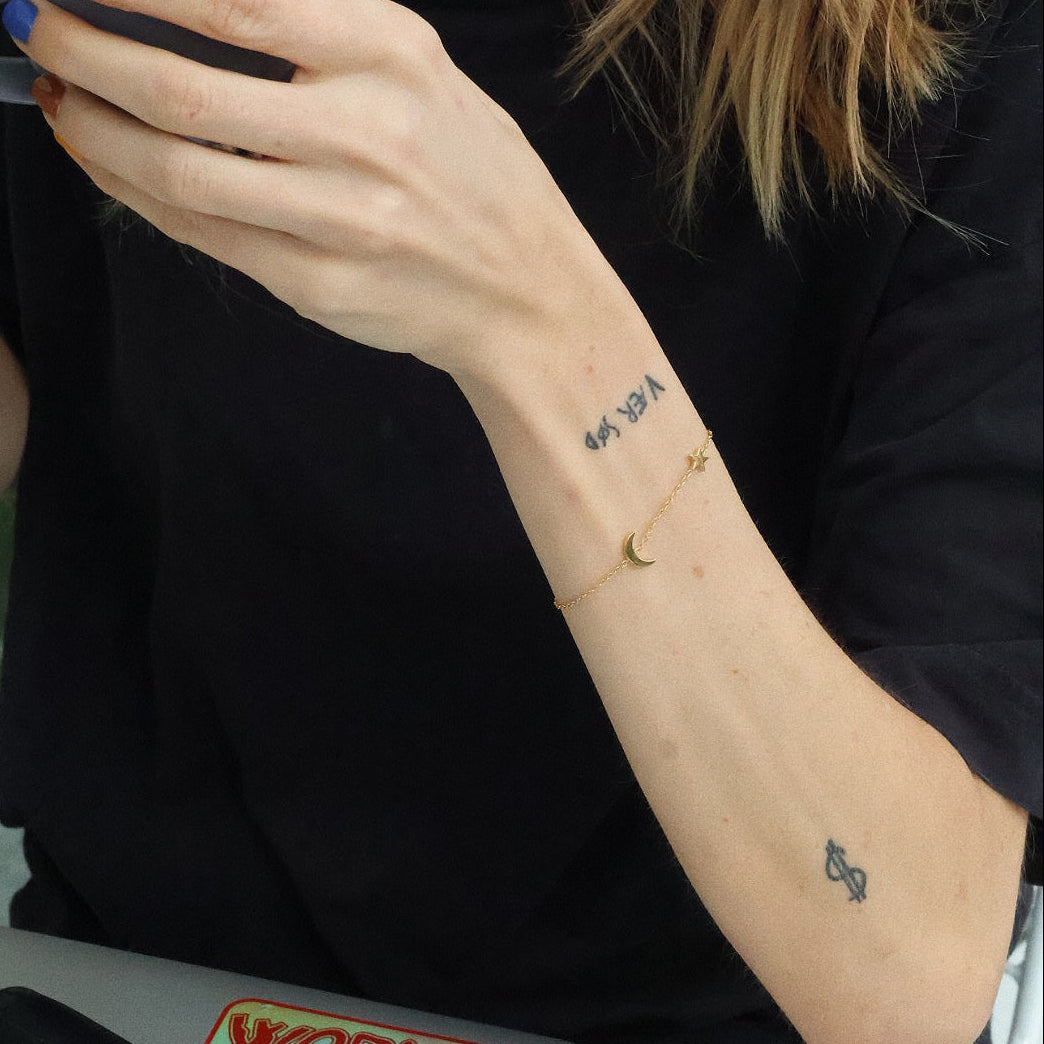 Thea bracelet worn solo on wrist, showcasing star and moon charms on a delicate gold chain