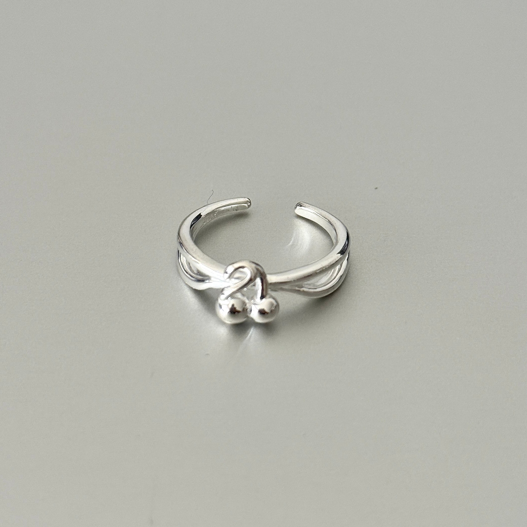 The Elara Ring, a minimalist S925 sterling silver band with a unique cherry-shaped silhouette, being worn on a finger.