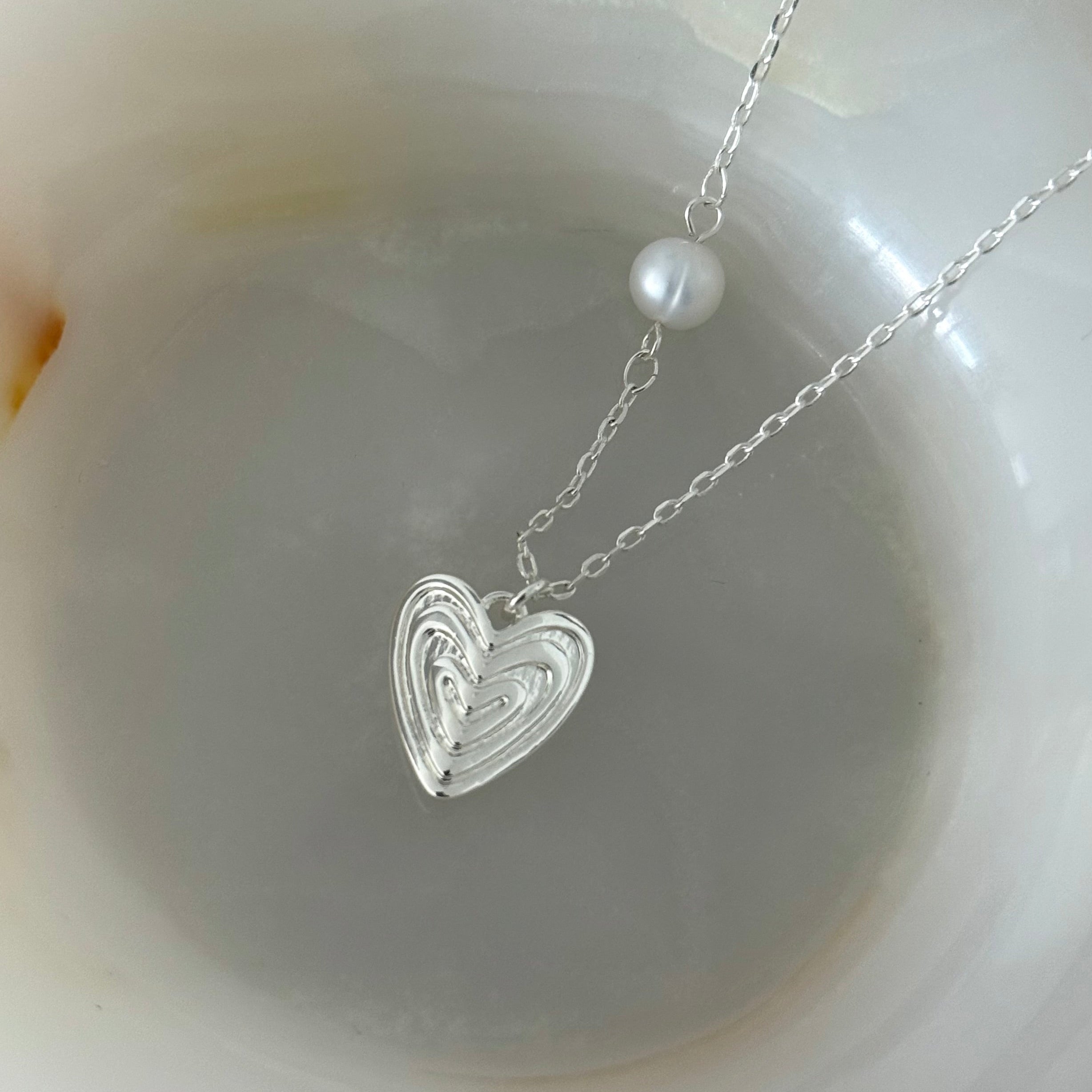 Close-up of the Veda necklace's layered heart pendant in white gold plating, highlighting intricate texture and pearl detail